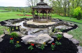 Koi pond surrounding gazebo built by Certified Aquascape Contractor Kingdom Landscaping in Mercersburg Pennsylvania featuring a biofalls filtration system and signature series skimmer with moat style pond stream and waterfall